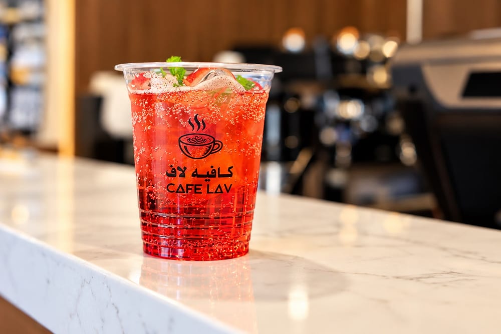 كوب مشروب أحمر فوّار مع شرائح الفراولة وأوراق النعناع، مطبوع عليه شعار كافيه لاف ⁦CAFE LAV⁩