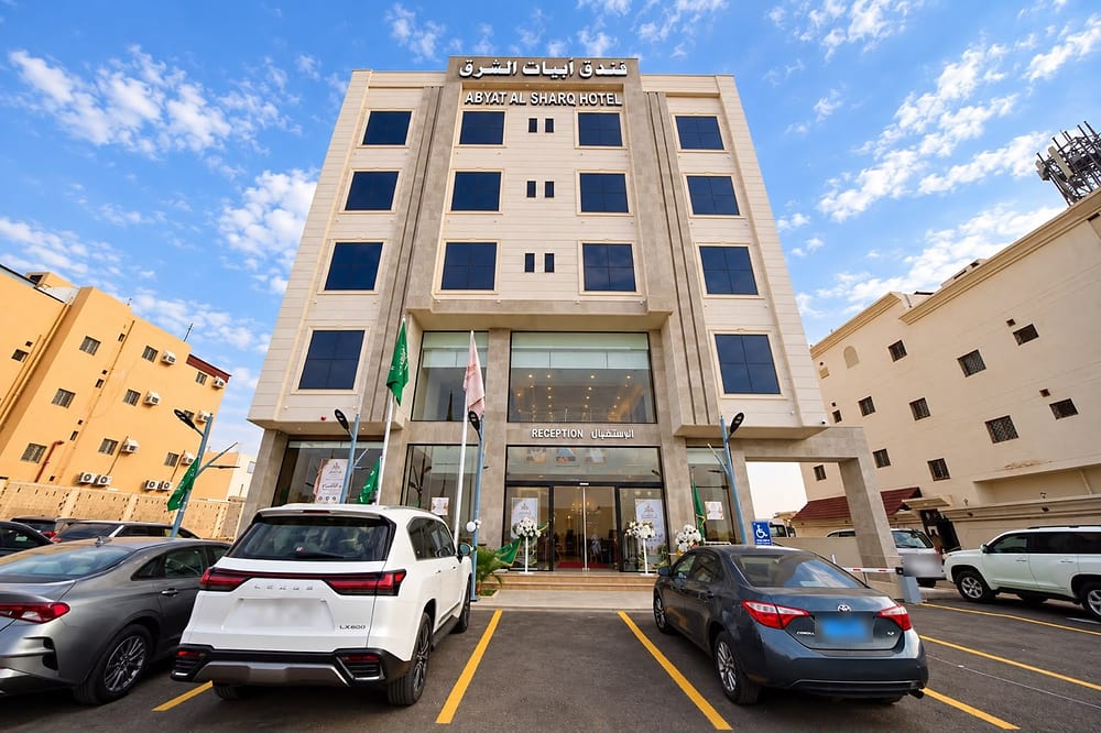 واجهة الفندق الحجرية بلون البيج بنوافذ زرقاء داكنة، ولافتة «فندق أبيات الشرق» ومدخل الاستقبال الزجاجي، وسيارات في الموقف