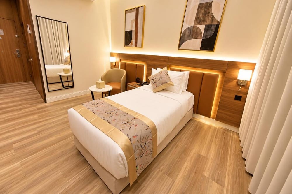 Double Room – Disability Access: single bed in white linen with a gold runner beside a small table and armchair