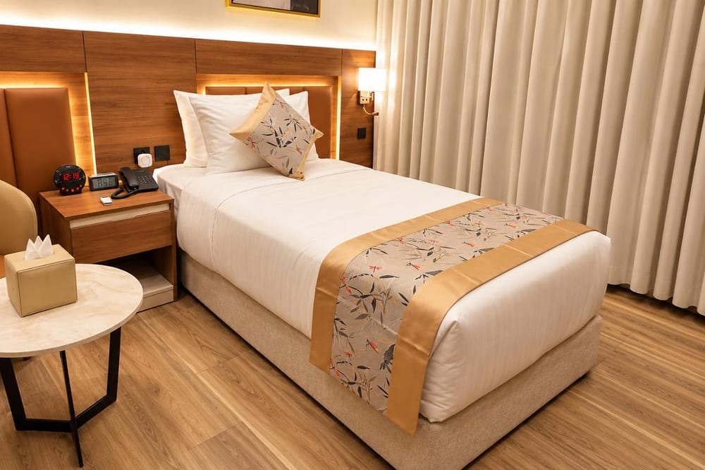 Double Room – Disability Access: single bed in white linen with a gold runner beside a small table and armchair